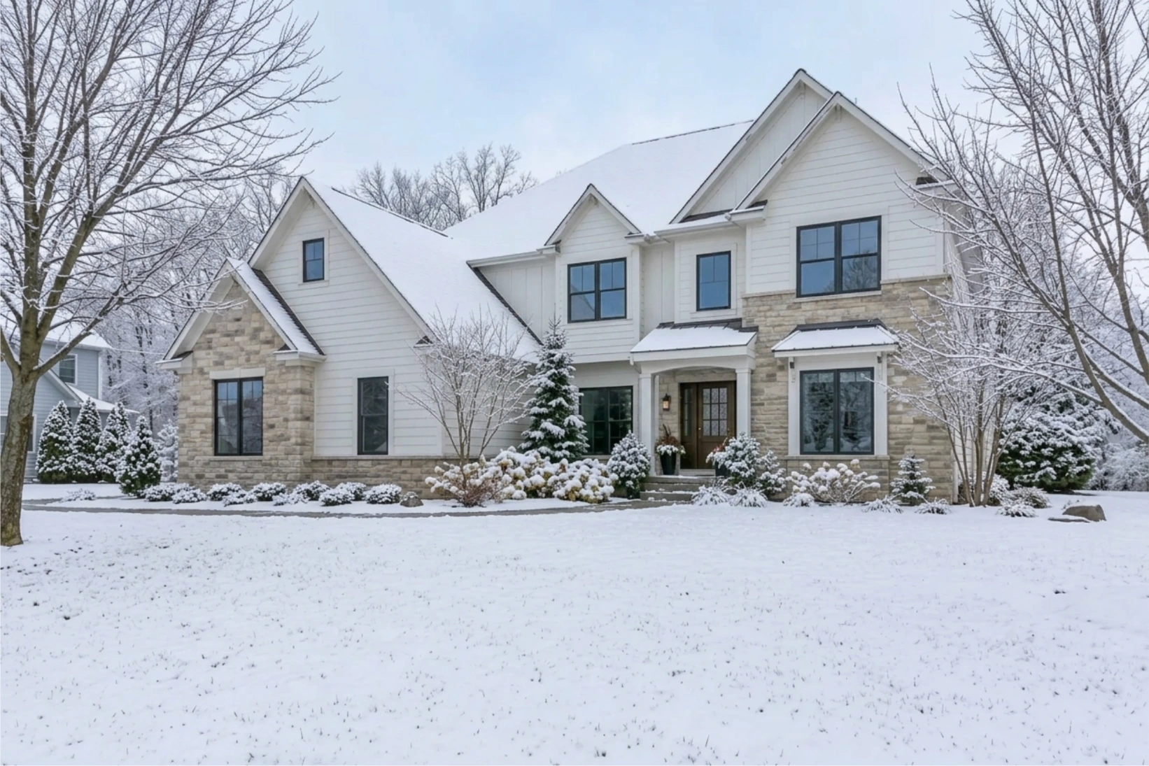 The house in a winter scene with snow on the lawn and roof and bare trees