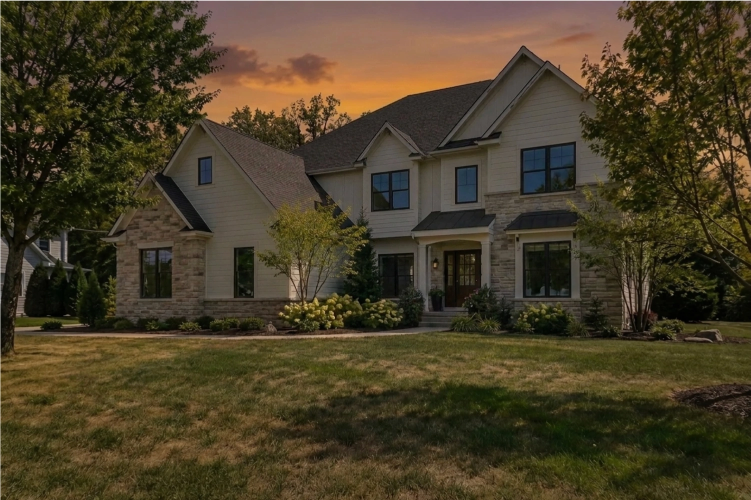 The same house under an orange sunset sky with the facade and lawn in evening light